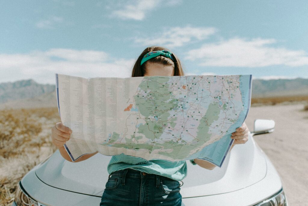 woman-looking-at-a-map while sitting on a car - how to make road trips more fun