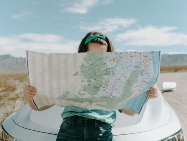 woman-looking-at-a-map while sitting on a car - how to make road trips more fun