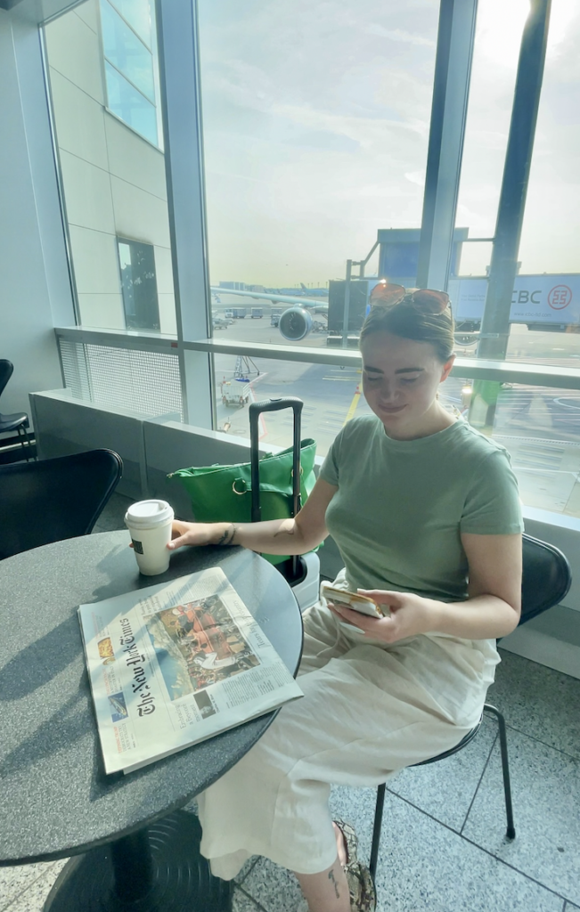 girl scrolling phone in airport lounge with luggage and bright windows